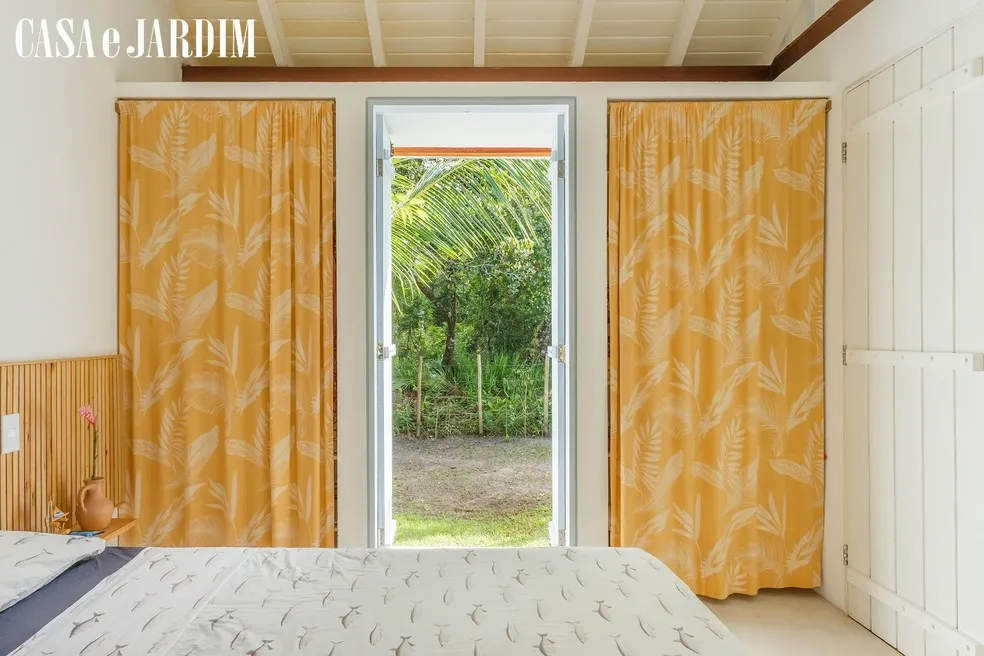Quarto com cortina amarela e porta para a mata