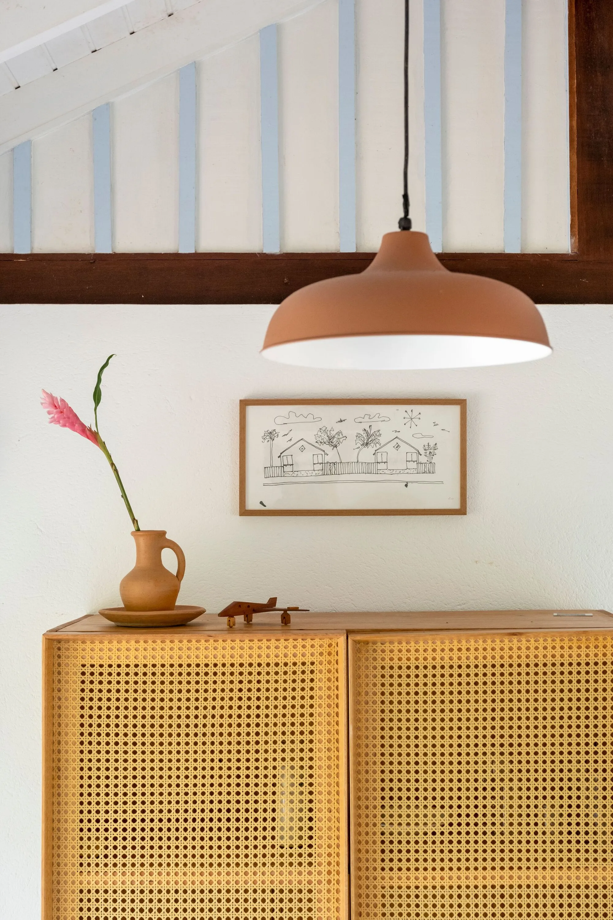 Buffet de palhinha sob a luminária de metal, com quadro na parede