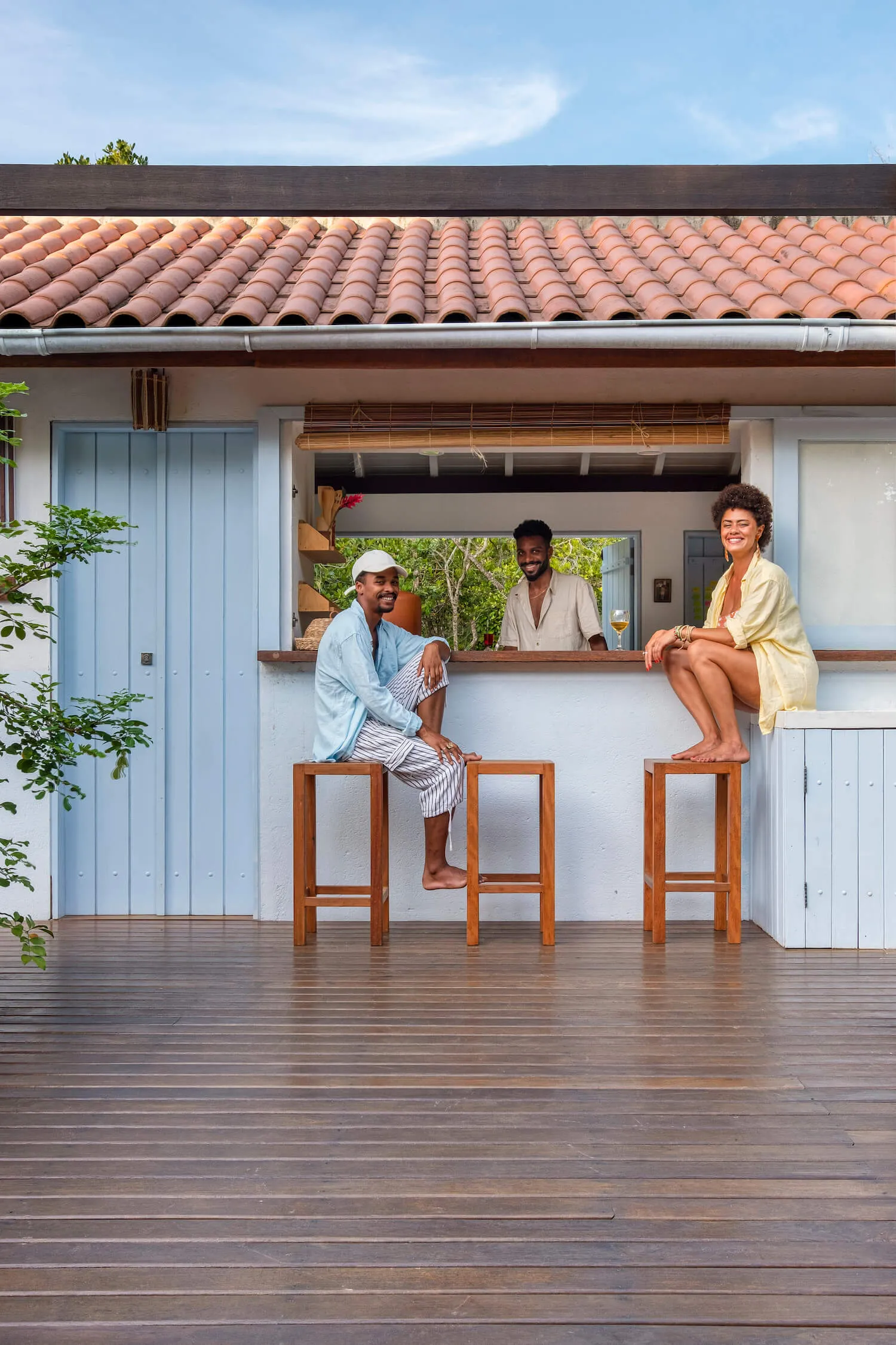 Fachada azul com dois moradores sentados no balcão que dá para o deck